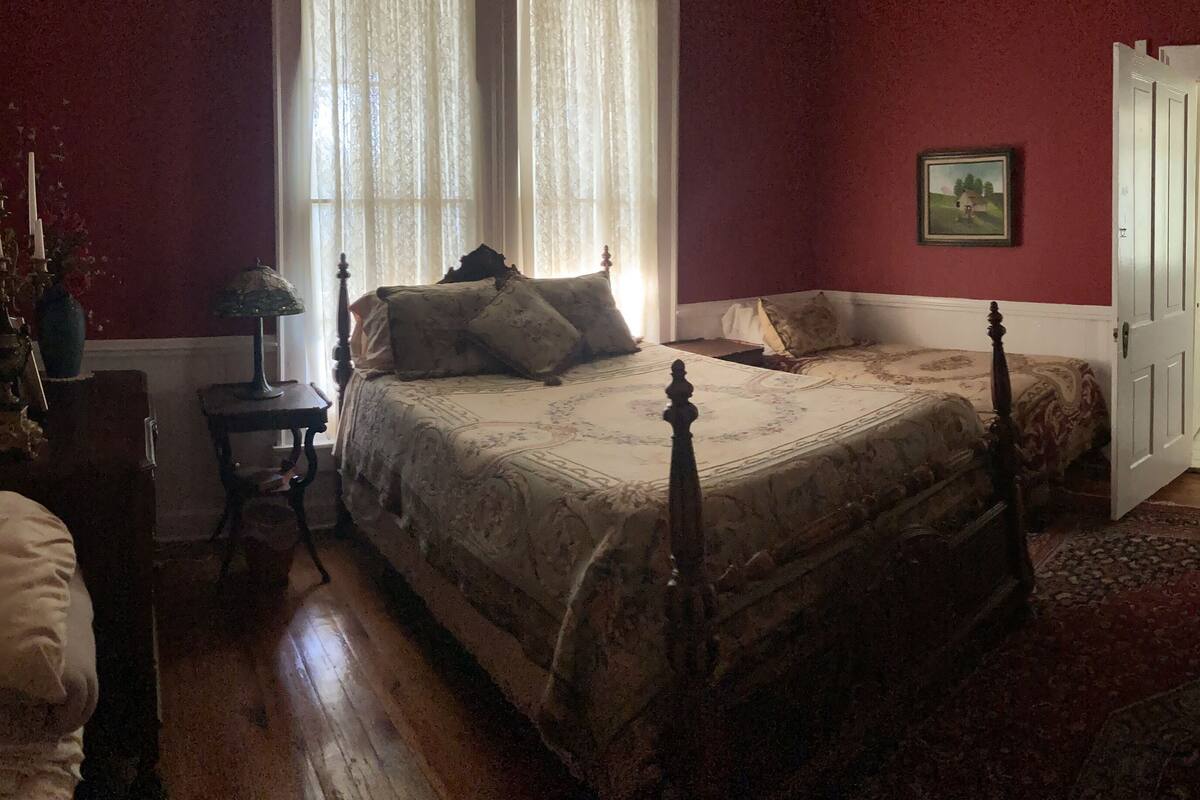 A traditional bedroom with a four-poster bed, a wooden nightstand, a mirror, and a red carpet.