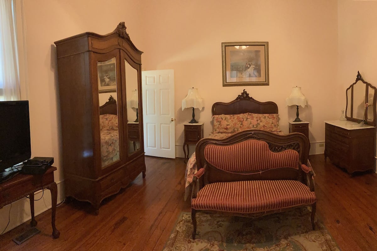A bedroom with a wooden bed, a wooden wardrobe, a television, and a dresser.