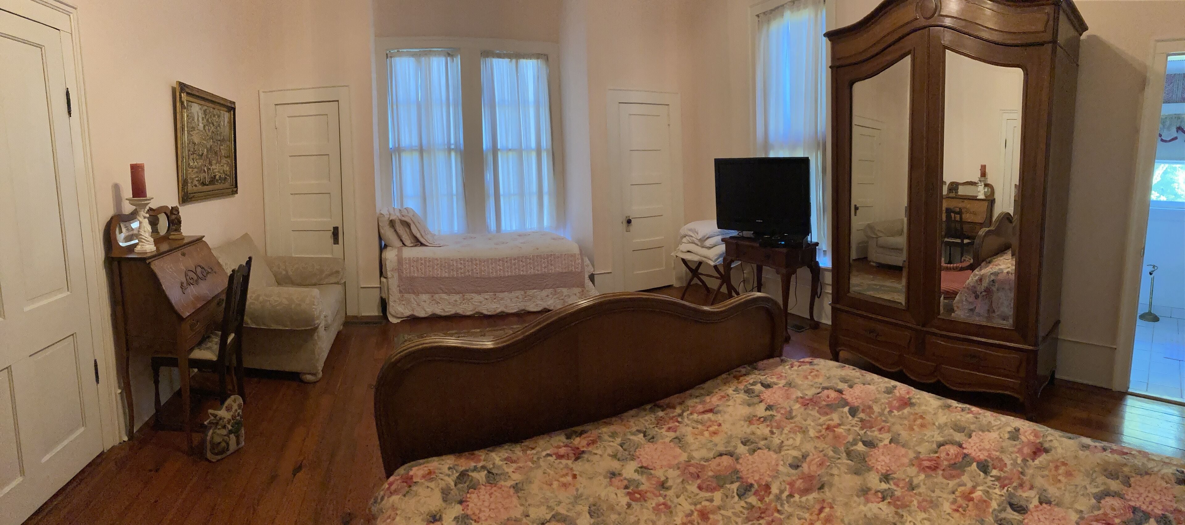 Een slaapkamer met een houten bed, een dressoir, een televisie en een spiegel.