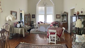 A spacious living room with a large arched window, a chandelier, and a dining area with a table set for two.