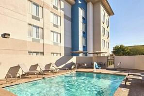 A swimming pool with lounge chairs and umbrellas, surrounded by a building with multiple windows and a door. - Springhill Suites By Marriott Phoenix Glendale Peoria (Glendale)