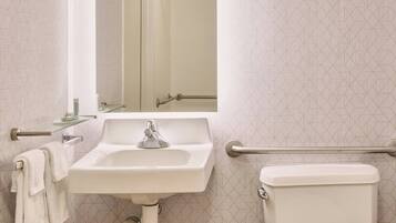 A bathroom with a sink, mirror, toilet, and grab bars.