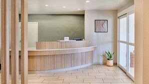 A reception desk with a modern design, a potted plant, and a large window providing natural light.