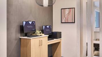 A modern office space with two computer monitors on a desk, a decorative pendant light, and a framed abstract painting on the wall.