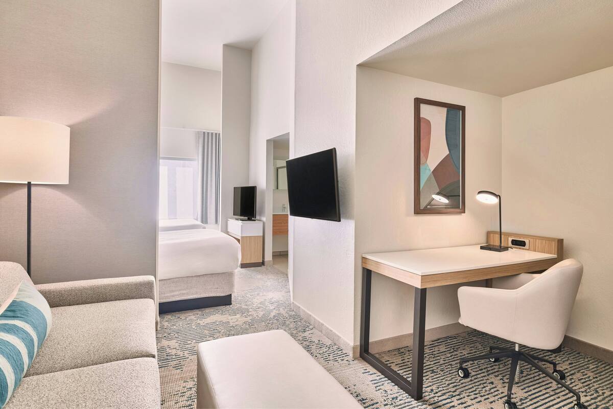Una habitación de hotel con cama, escritorio, silla, televisor y lámpara.