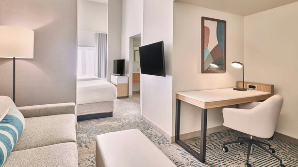A hotel room with a bed, a desk, a chair, a TV, and a lamp.