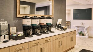 A coffee station with multiple dispensers, a mirror, and a framed artwork on the wall.