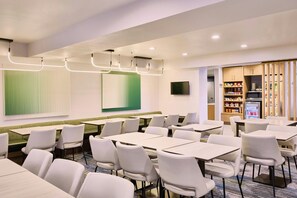 A modern dining area with tables and chairs, a television, and a vending machine. - Springhill Suites By Marriott Phoenix Glendale Peoria (Glendale)