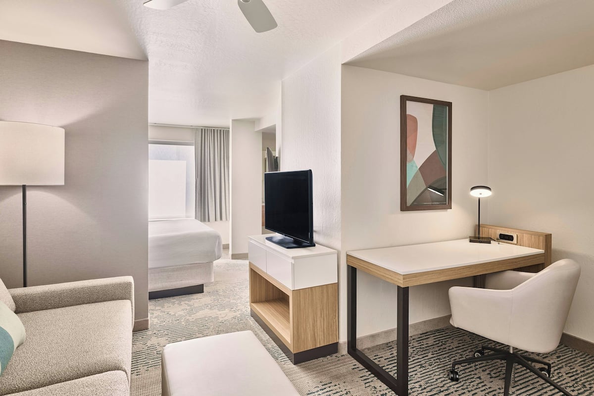 Una habitación de hotel moderna con una cama, un escritorio, una silla, un televisor y una lámpara.