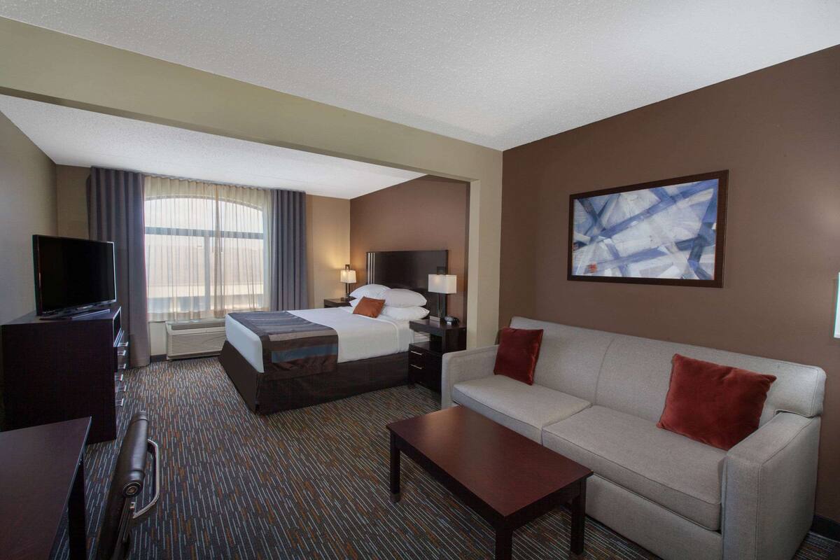 Ein Hotelzimmer mit Bett, Sofa, Fernseher und einem Gemälde an der Wand.
