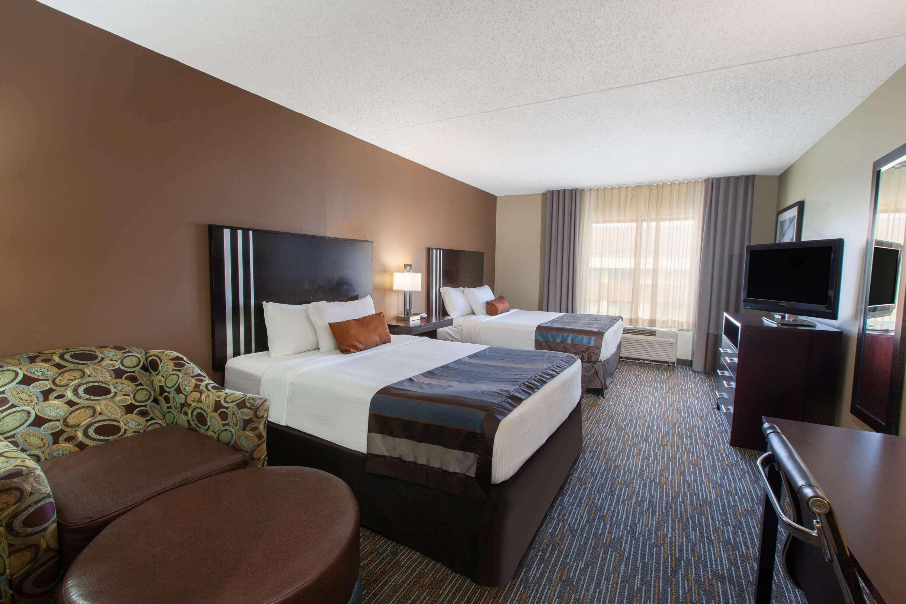 A hotel room with two beds, a sofa, a desk, and a TV.