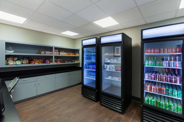 Una kitchenette con tres dispensadores de bebidas repletos de diversas opciones, una encimera con aperitivos y armarios con utensilios de cocina.