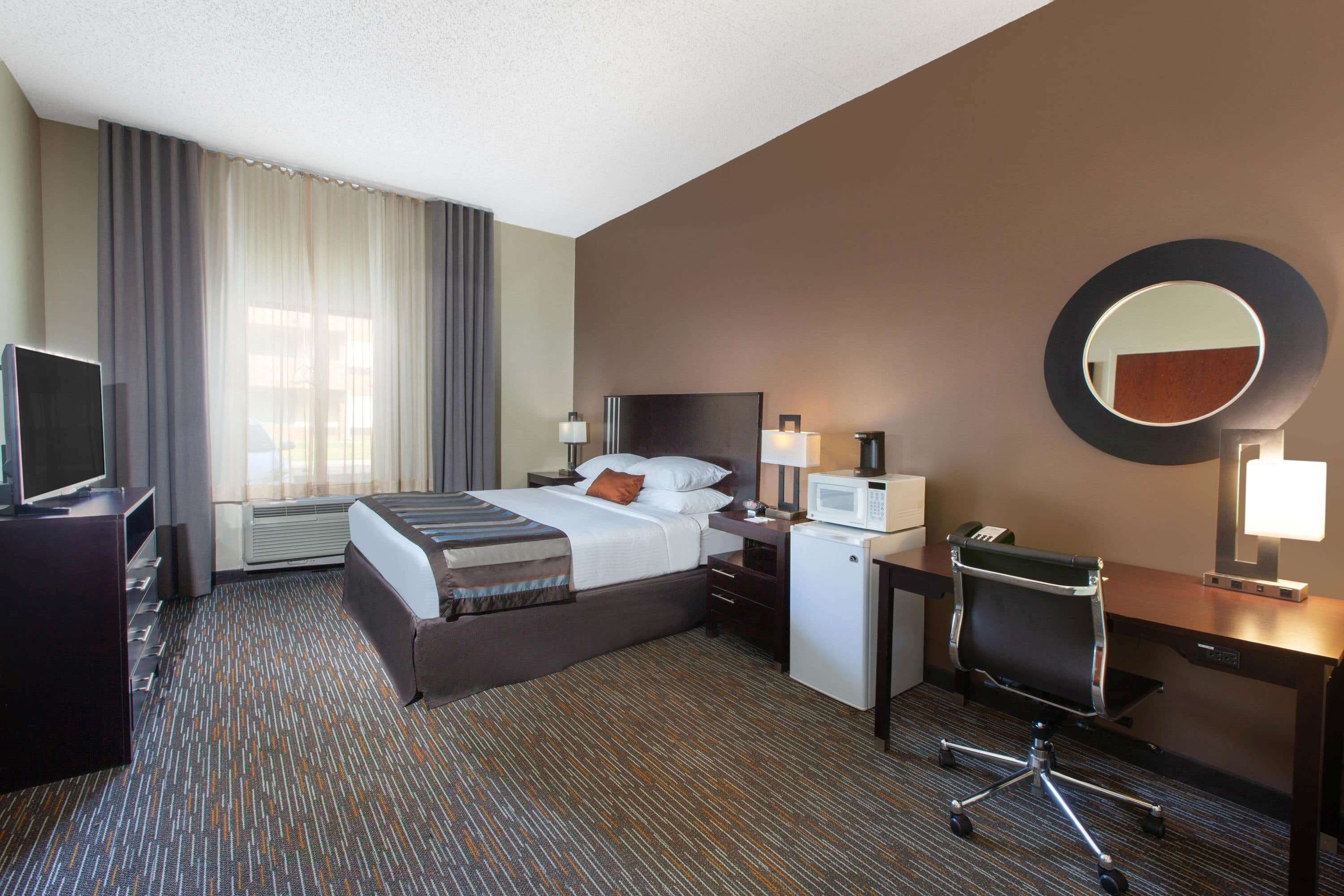 A hotel room with a bed, desk, chair, TV, and a microwave.