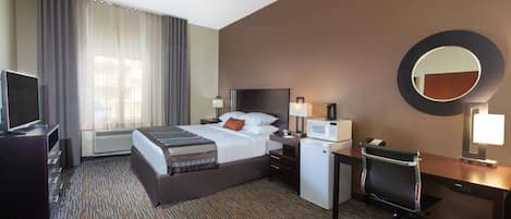 A hotel room with a bed, desk, chair, TV, and a microwave.