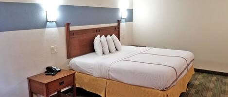 A hotel room with a single bed, a wooden nightstand with a telephone, and a small drawer.