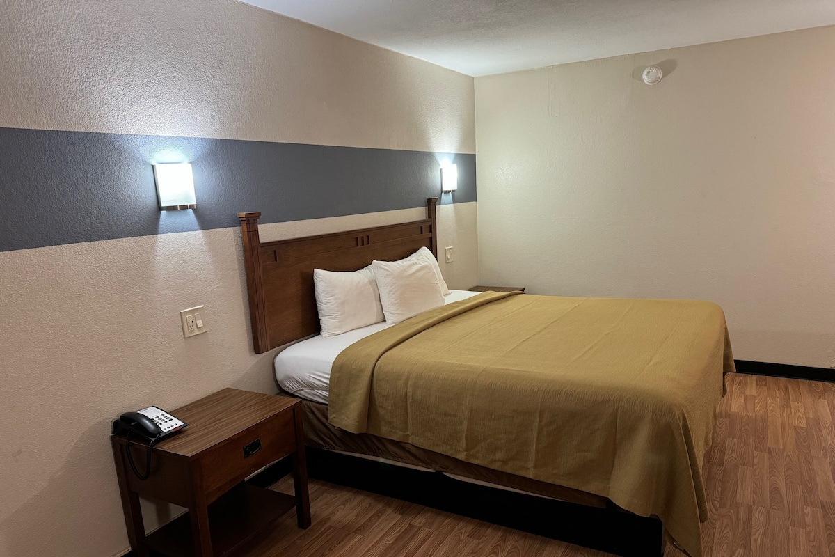 A hotel room with a bed, bedside table, and a wall-mounted light fixture.