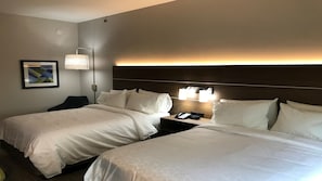 A hotel room with two beds, a nightstand with a phone, and a wall-mounted light fixture.