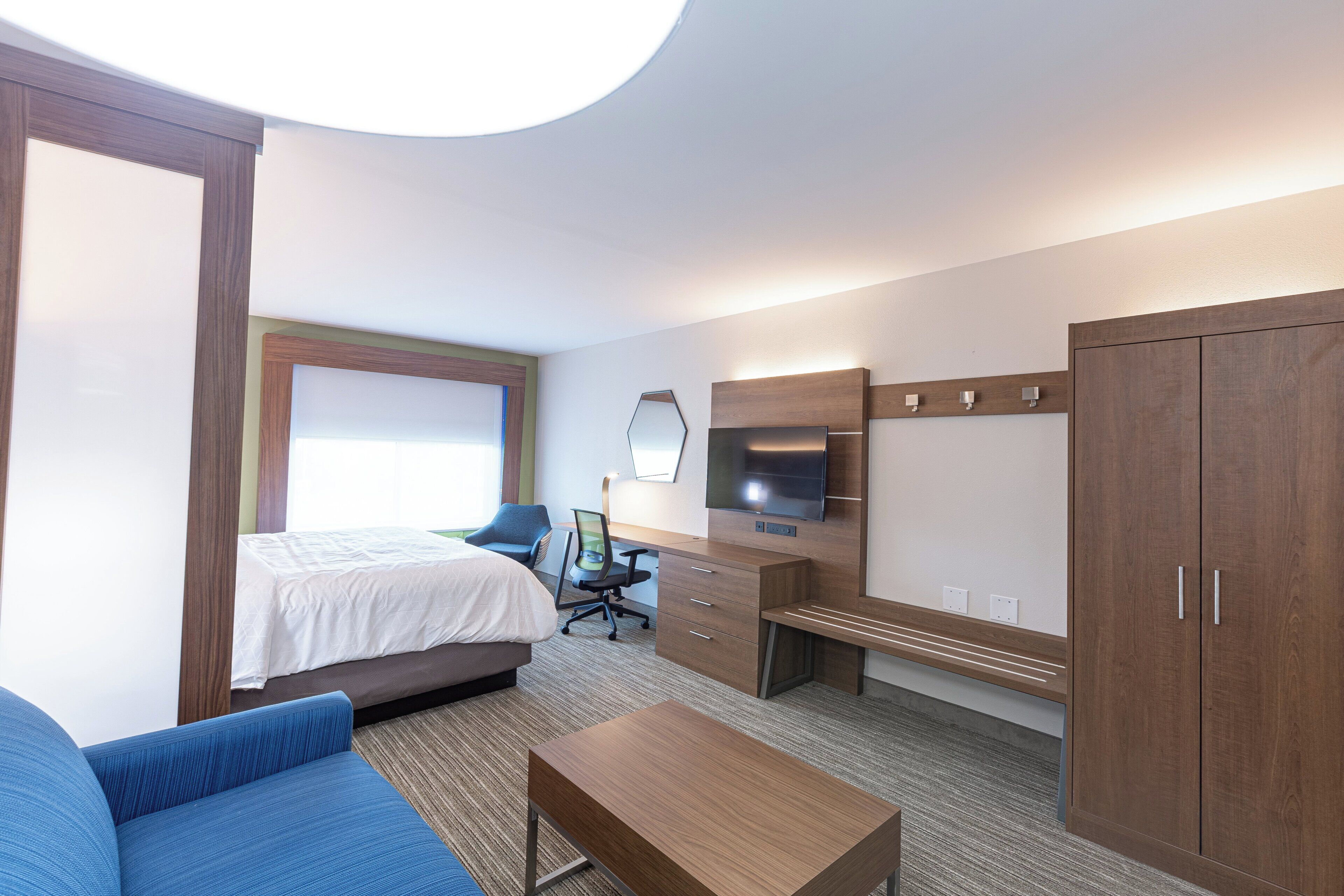 A hotel room with a bed, a desk, a television, a wardrobe, and a sofa.