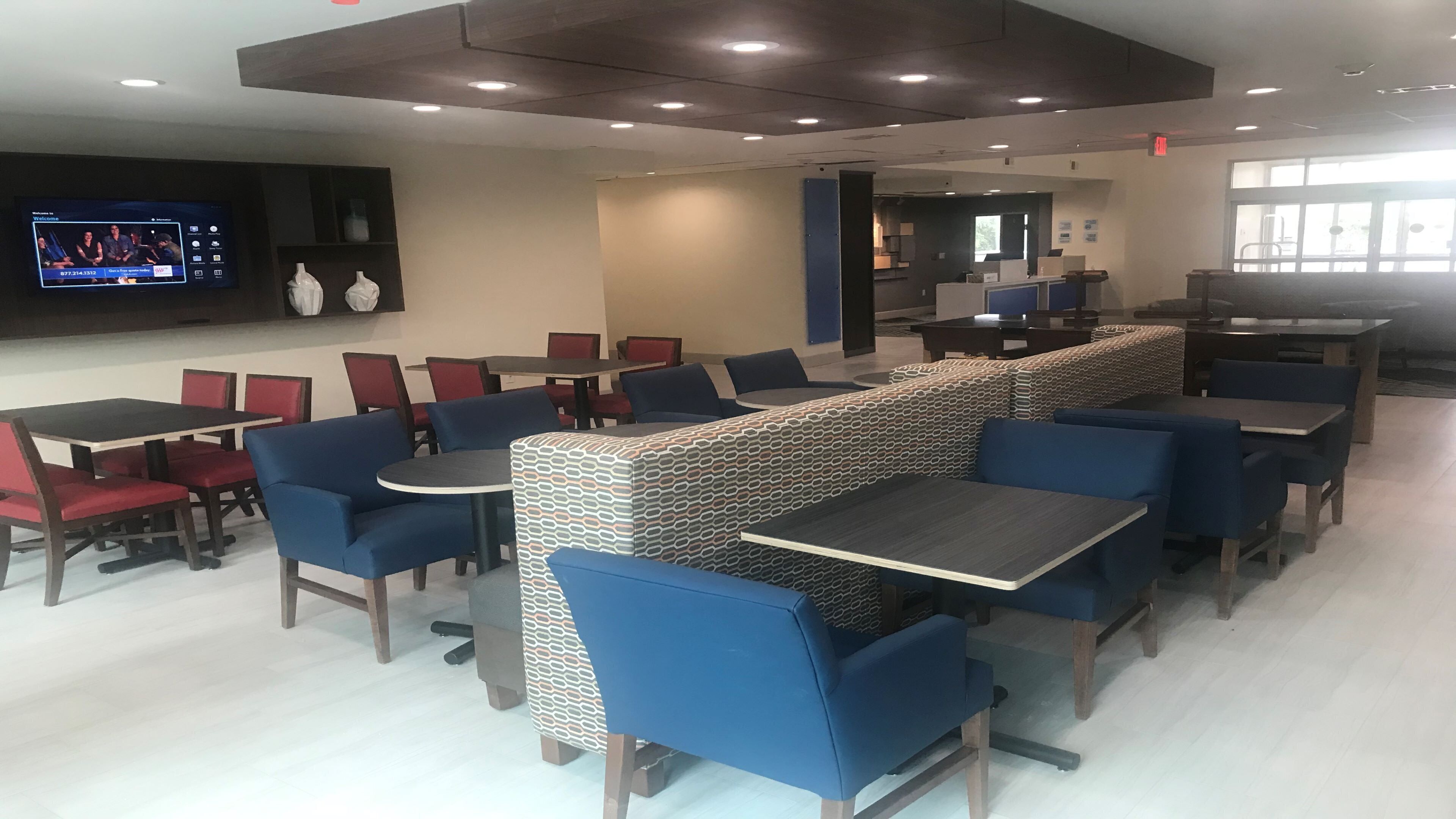 A modern dining area with multiple tables and chairs, a television screen, and a patterned bench.