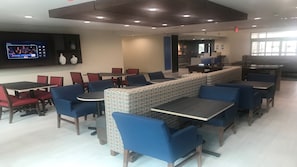 A modern dining area with multiple tables and chairs, a television screen, and a patterned bench. - Holiday Inn Express & Suites Arlington North - Stadium Area by IHG (Arlington)