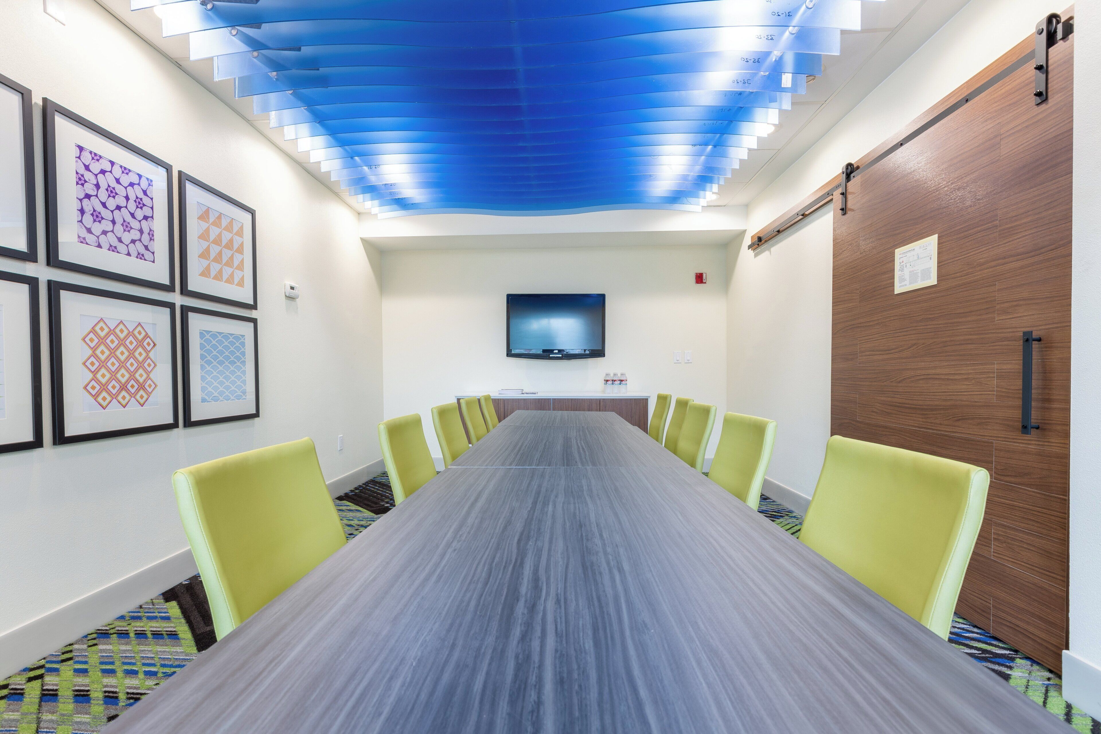 A conference room with a long table, yellow chairs, a flat-screen TV, and framed artwork on the walls.
