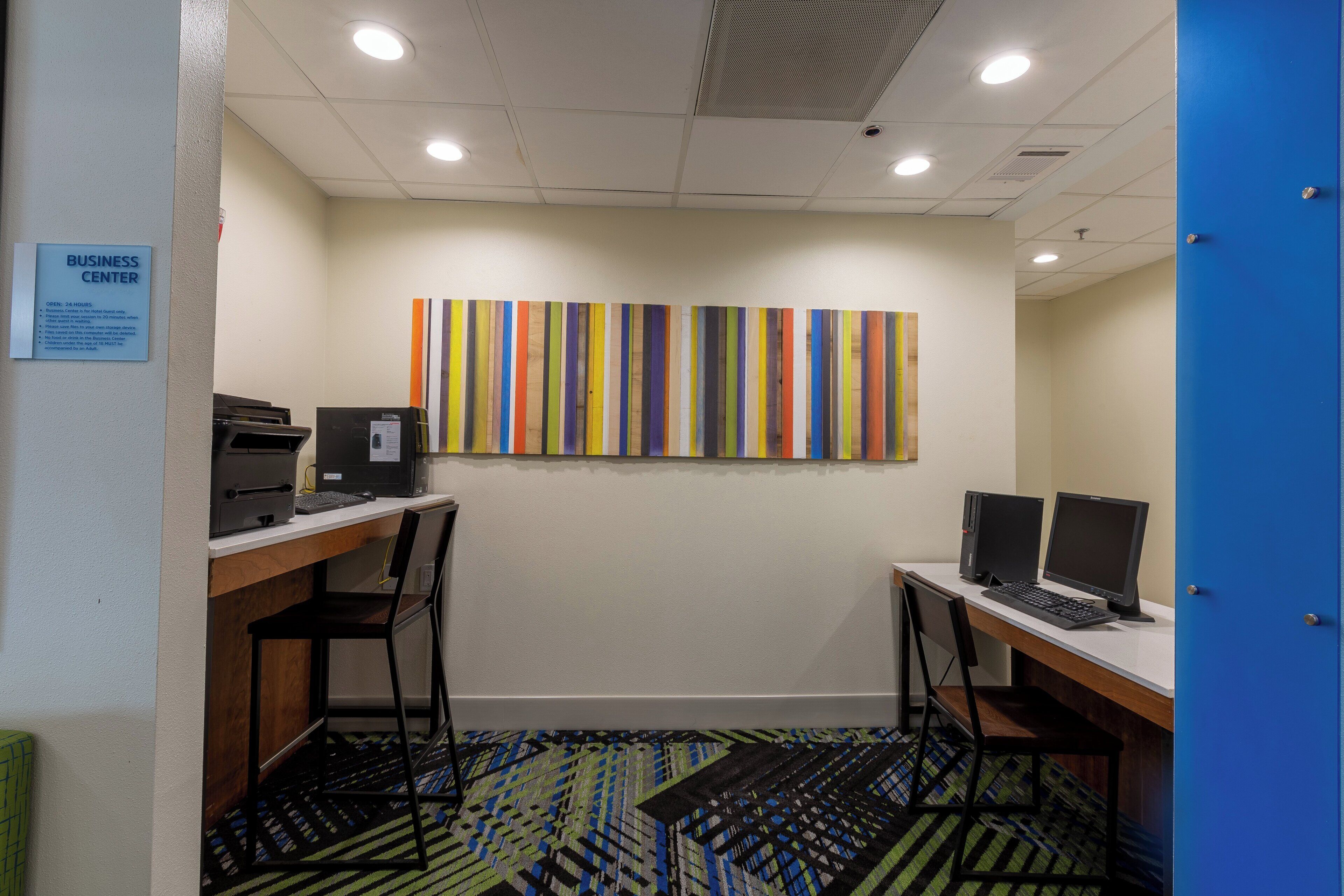 Centro de negocios con dos estaciones de computadora, un cuadro abstracto y colorido en la pared, y un letrero que indica que es solo para huéspedes del hotel.