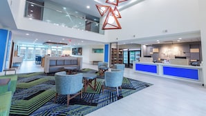 A spacious lobby with a high ceiling, a central seating area with sofas and chairs, and a reception desk with a blue accent wall. - Holiday Inn Express & Suites Arlington North - Stadium Area by IHG (Arlington)