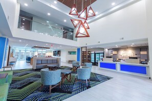 A spacious lobby with a high ceiling, a central seating area with sofas and chairs, and a reception desk with a blue accent wall. - Holiday Inn Express & Suites Arlington North - Stadium Area by IHG (Arlington)