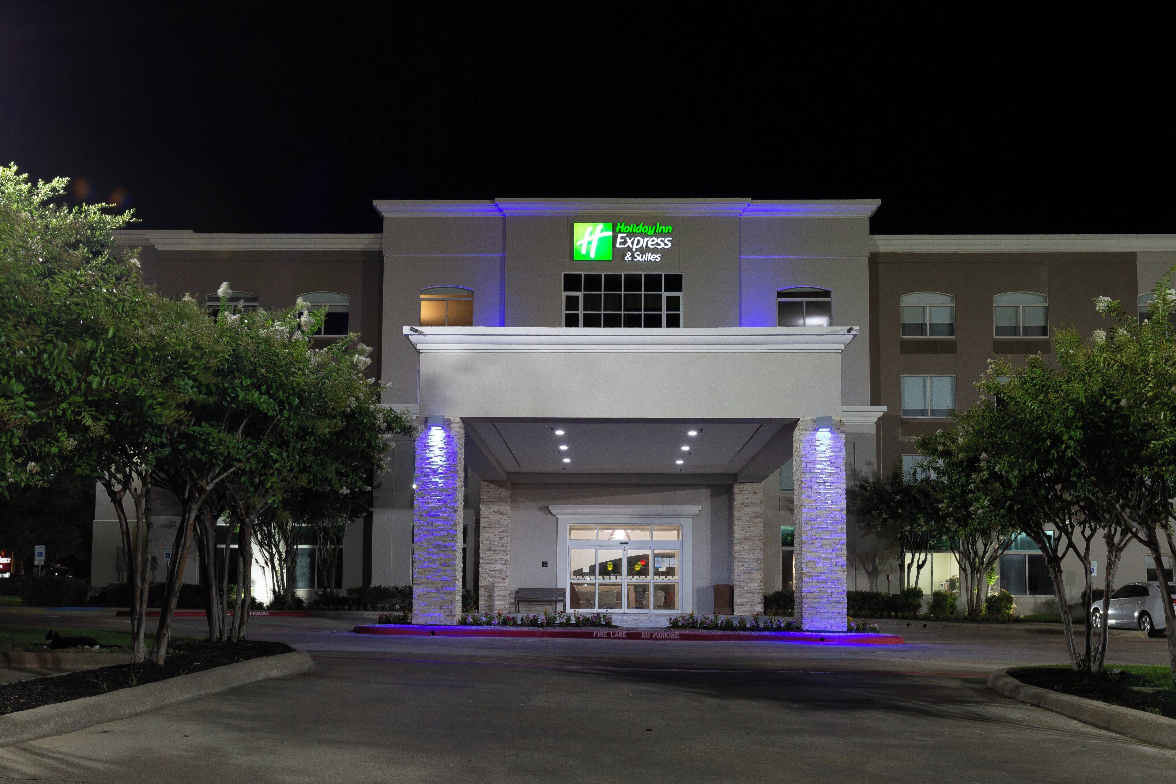 De ingang van een Holiday Inn Express & Suites hotel met een modern ontwerp, met een opvallend bord en een goed verlichte gevel.