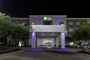 De ingang van een Holiday Inn Express & Suites hotel met een modern ontwerp, met een opvallend bord en een goed verlichte gevel.