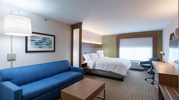A hotel room with a bed, a blue sofa, a wooden desk, and a large window.