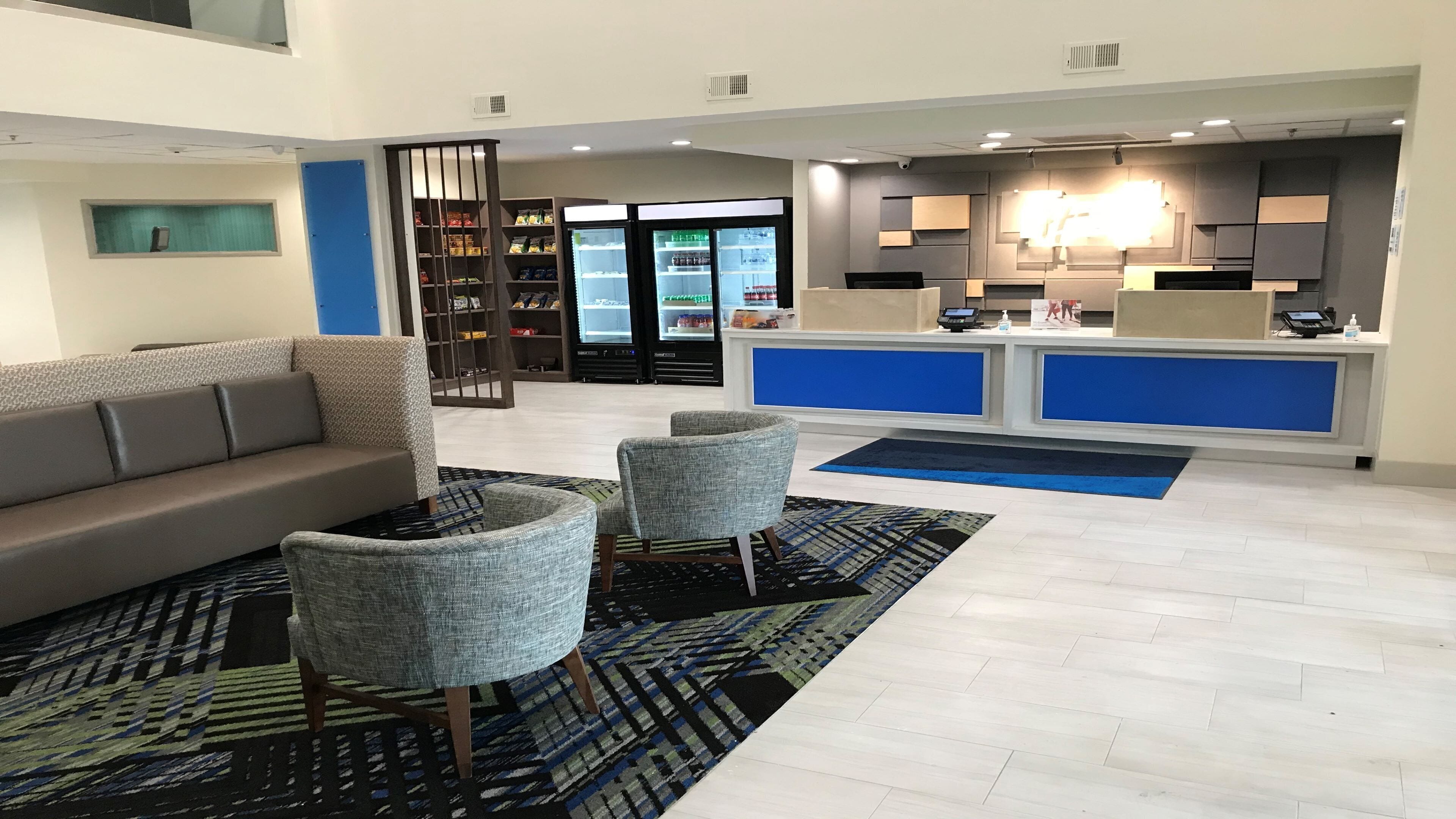 A hotel lobby with a reception desk, a sofa, two armchairs, a patterned rug, and a bookshelf.