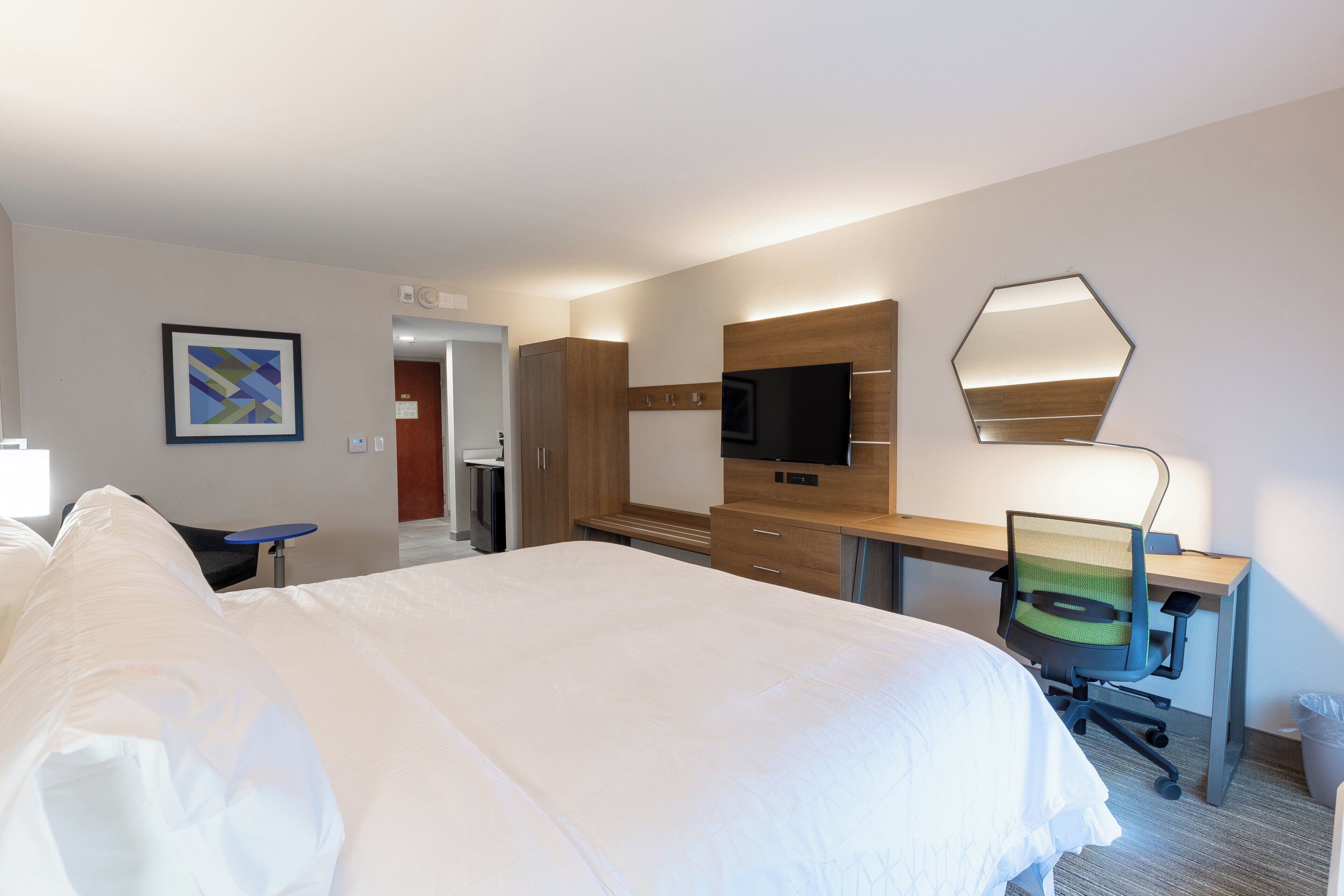 A hotel room with a large bed, a desk with a chair, a television, and a mirror.