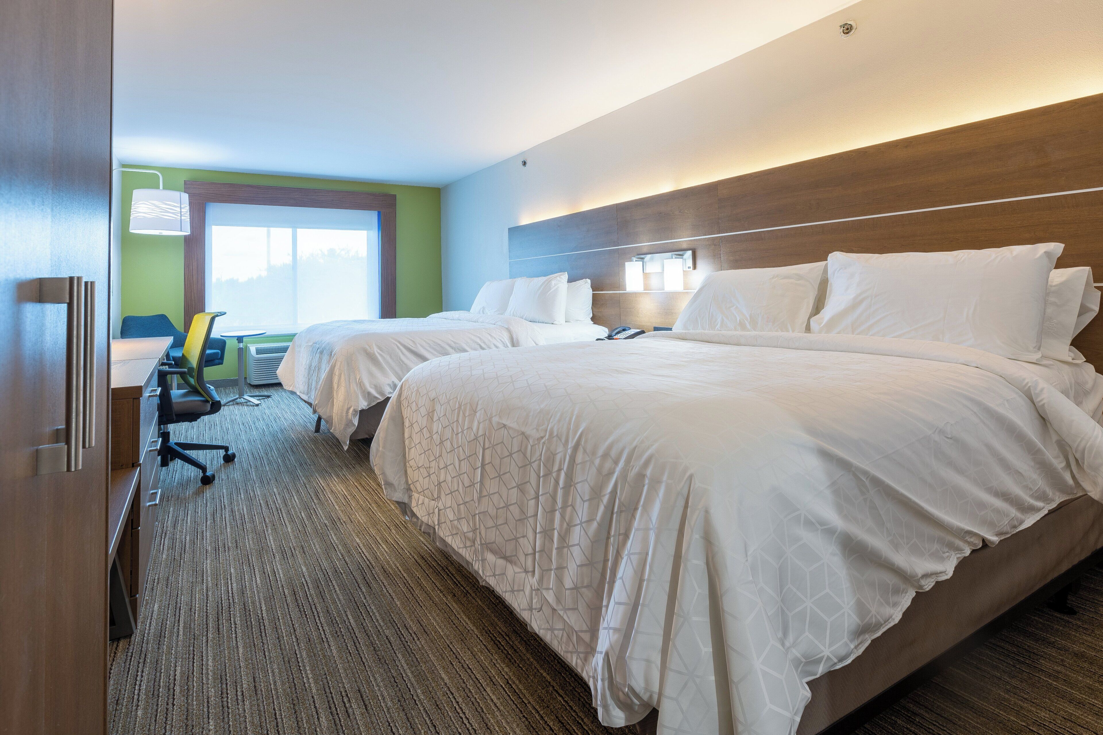 A hotel room with two beds, a desk, a chair, and a window.
