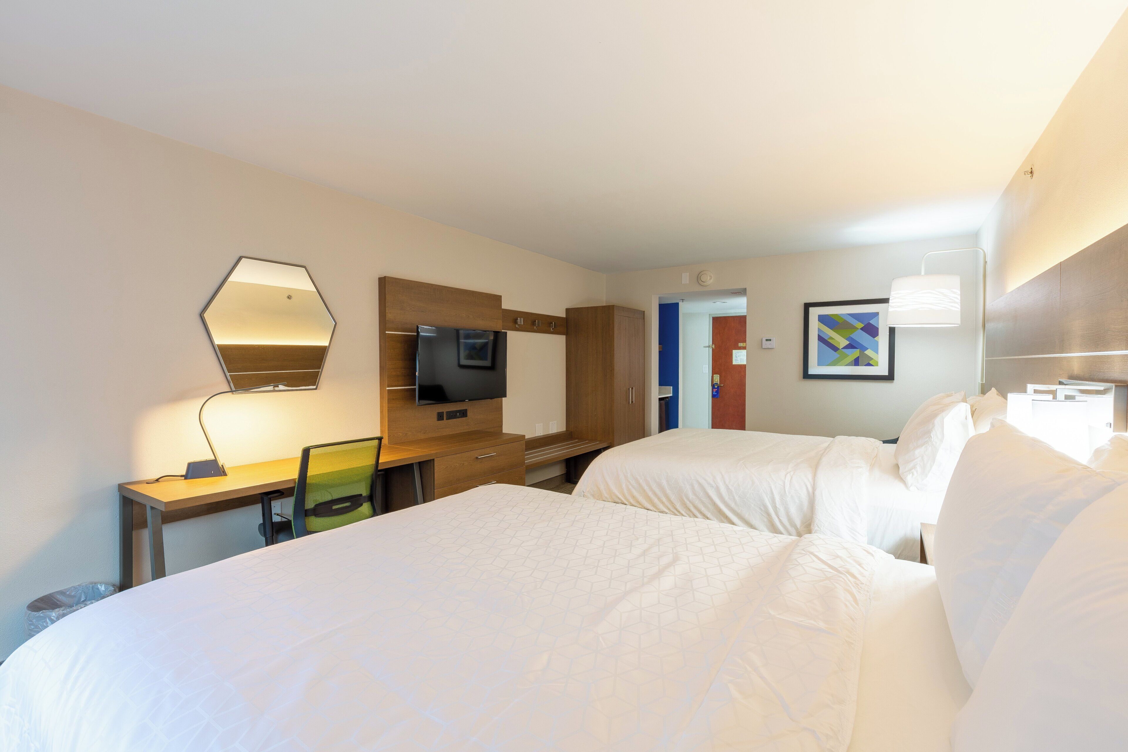 Une chambre d’hôtel avec deux lits, un bureau avec un ordinateur, un téléviseur à écran plat et un miroir.