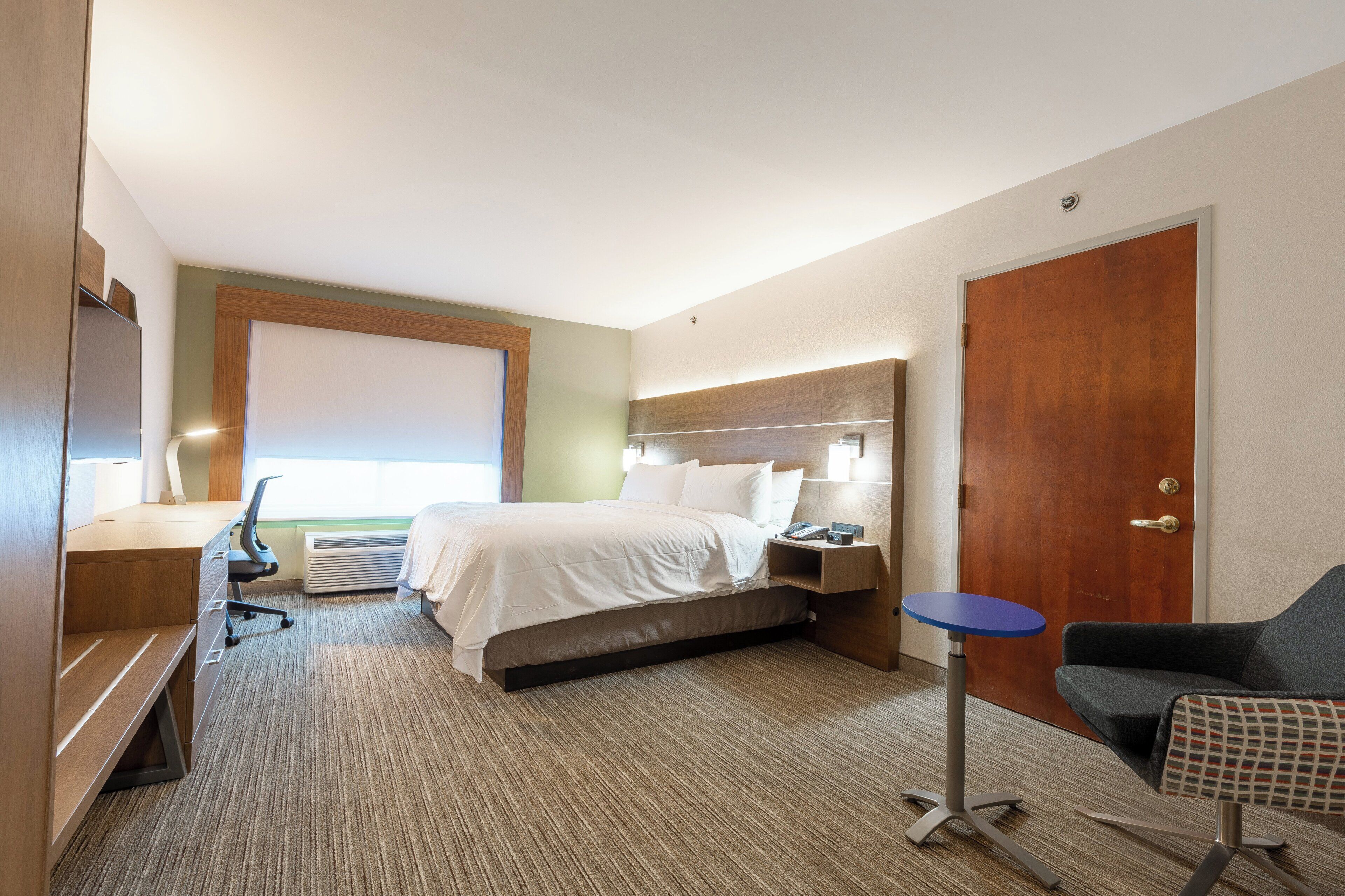 A hotel room with a bed, bedside table, chair, desk, and a television.