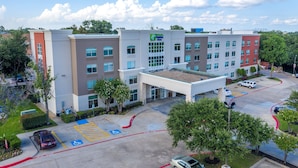 A multi-story hotel with a central entrance, parking lot, and surrounding greenery. - Holiday Inn Express & Suites Arlington North - Stadium Area by IHG (Arlington)