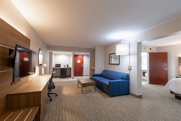 A hotel room with a wooden desk, a blue sofa, a small table, a TV, and a bed.