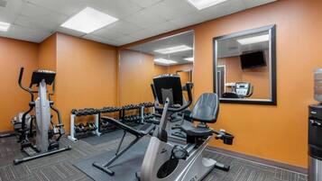 A gym with cardio equipment, dumbbells, and a mirror.