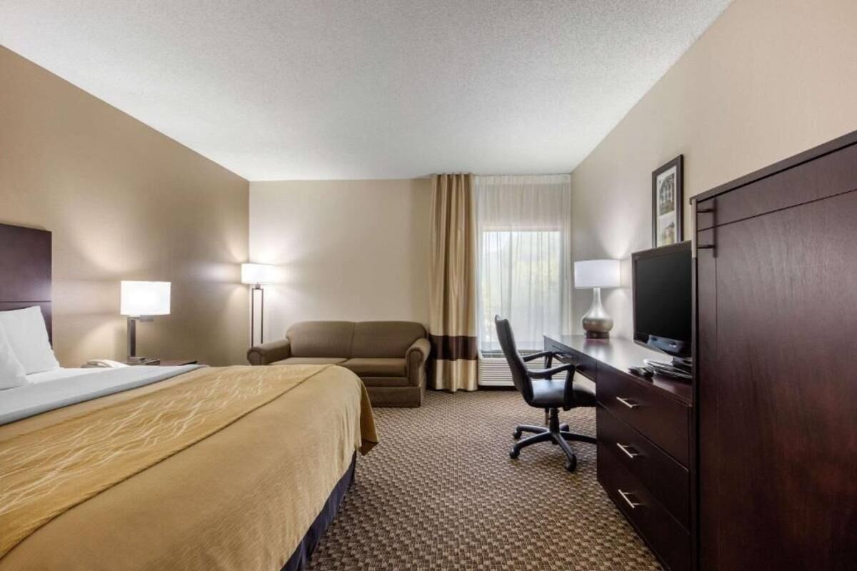 Een hotelkamer met een bed, een bureau, een stoel, een televisie en een kledingkast.