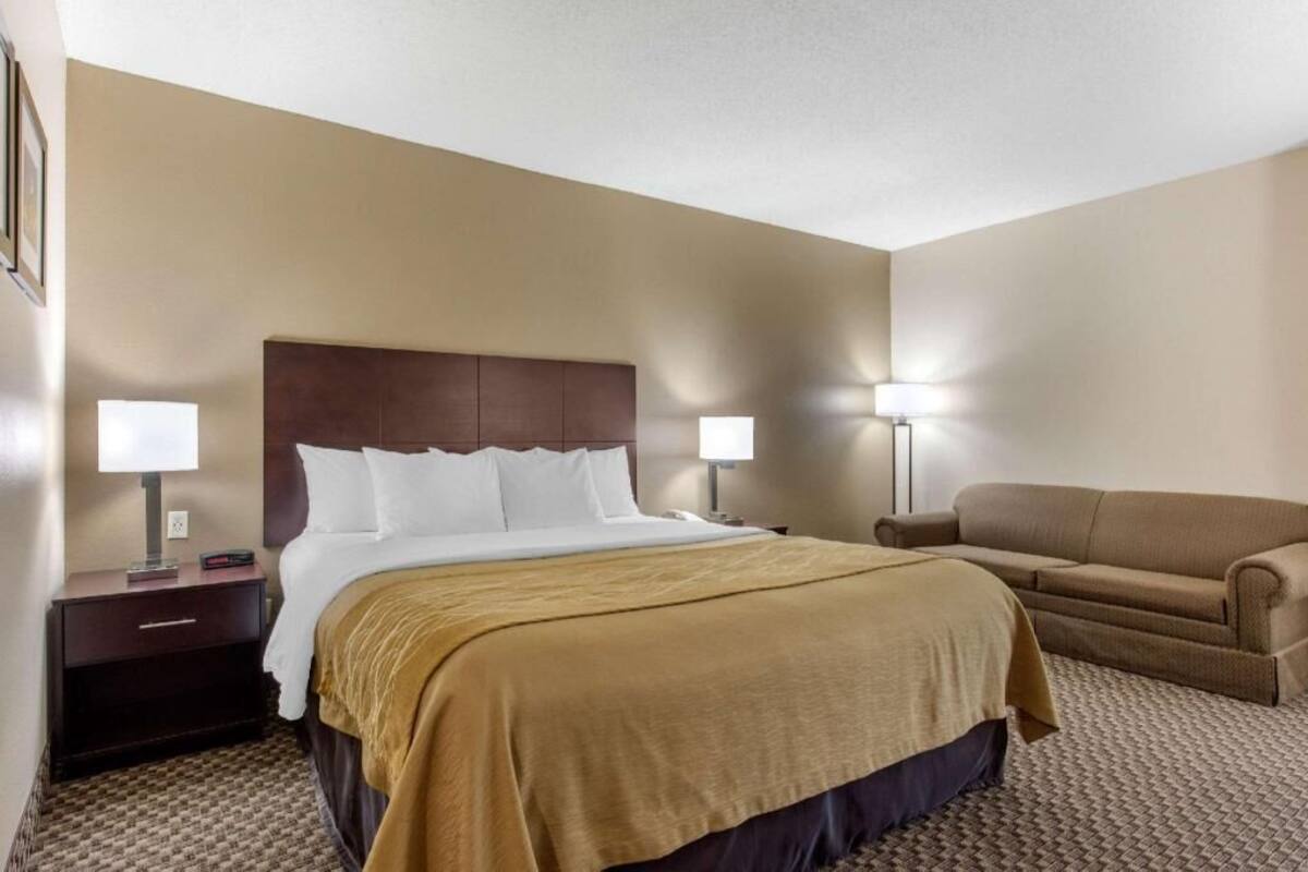 Een hotelkamer met een bed, nachtlampjes, een slaapbank en een nachtkastje.