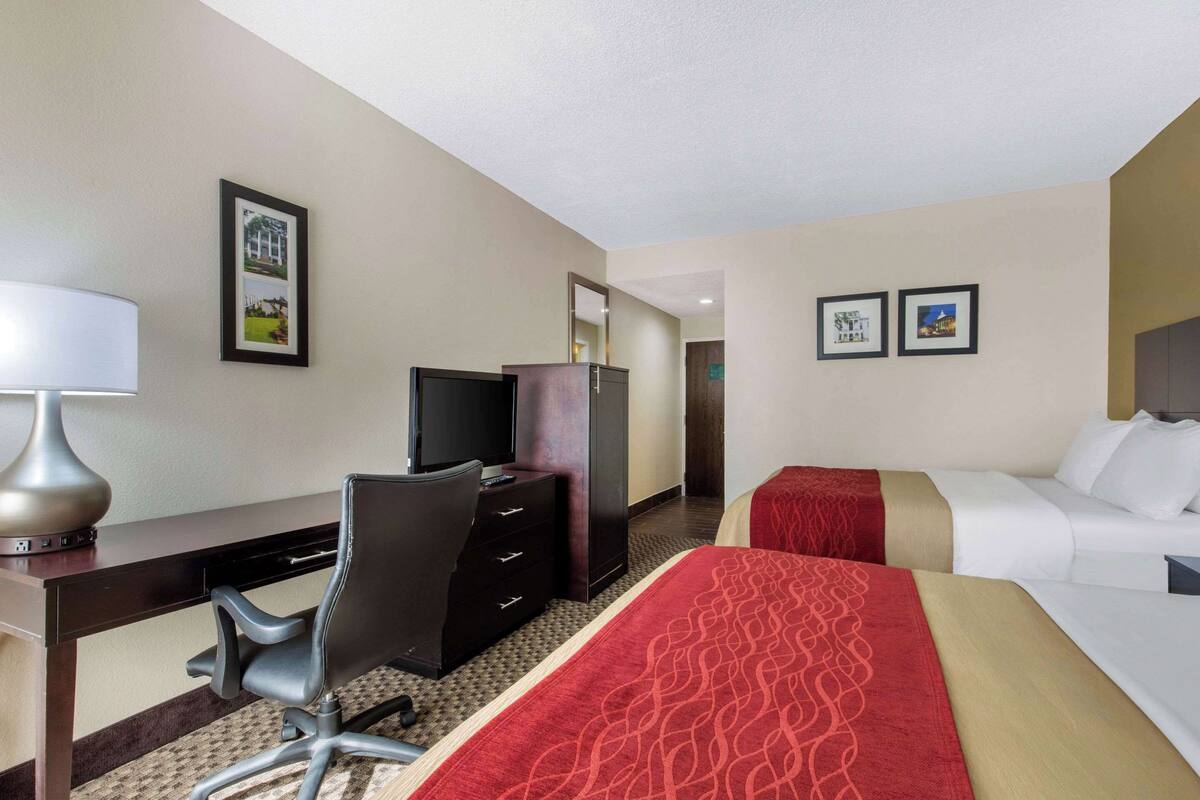 Een hotelkamer met een bureau, stoel, televisie, kledingkast en twee bedden.