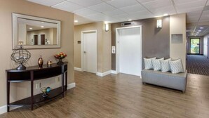 A hotel lobby with a wooden floor, a console table with decorative items, a sofa with patterned cushions, and a large mirror on the wall. - Comfort Inn Horn Lake - Southhaven (Horn Lake)