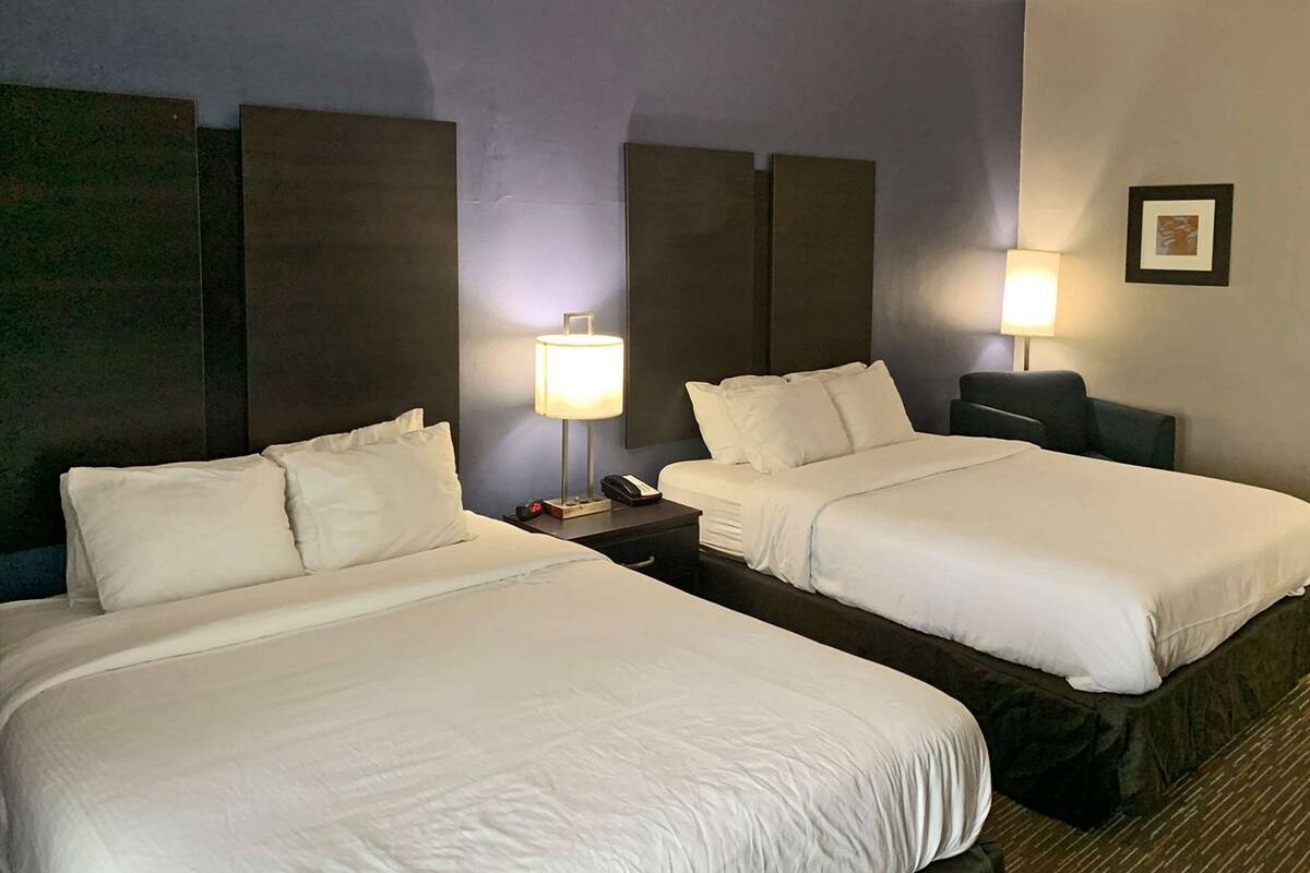 A hotel room with two beds, nightstands, lamps, and a framed picture on the wall.