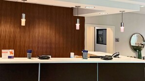 A reception desk with a wooden panel wall, a white counter, and a mirror on the right.
