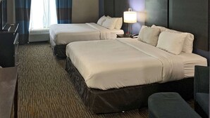 A hotel room with two beds, a desk, a chair, and a lamp.