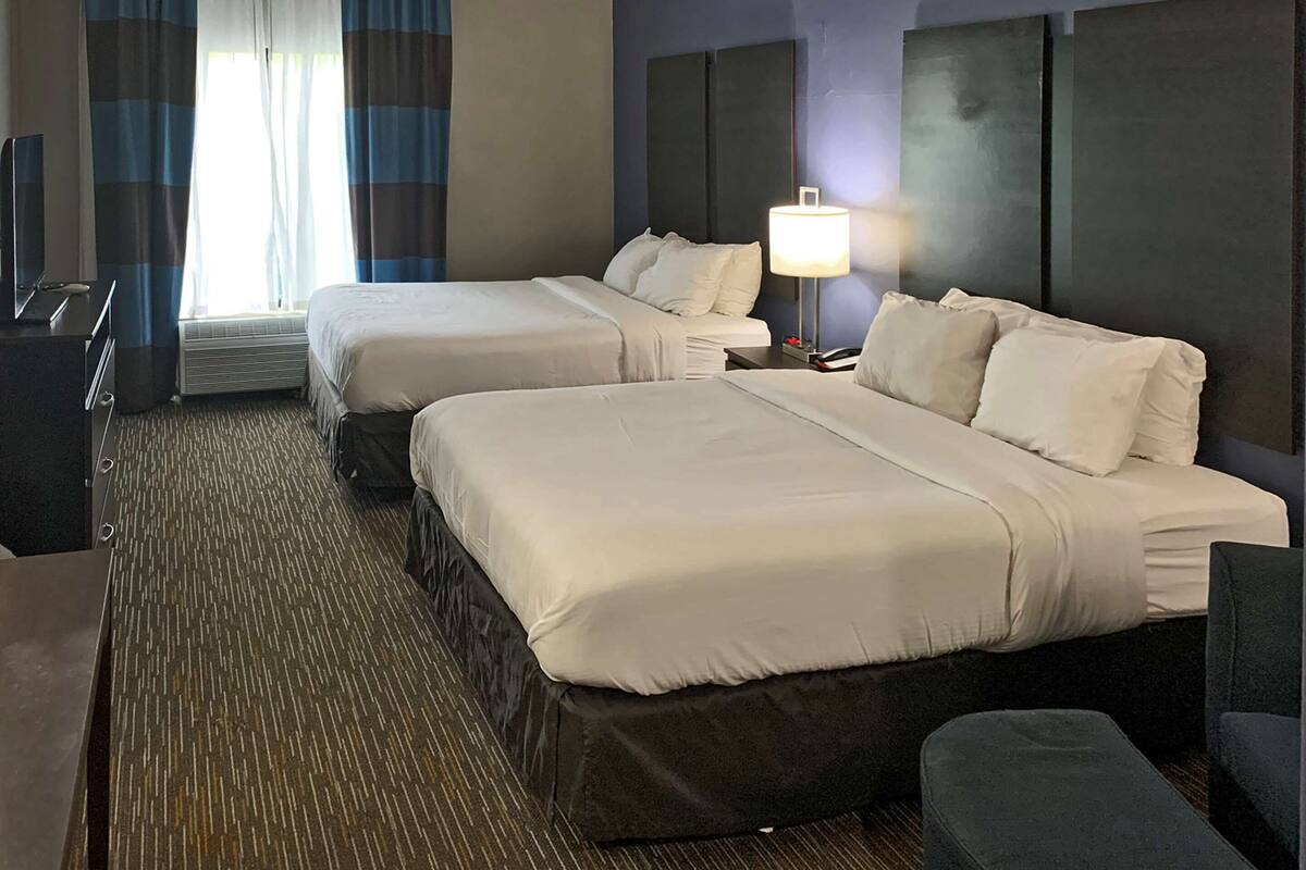 A hotel room with two beds, a desk, a chair, and a lamp.