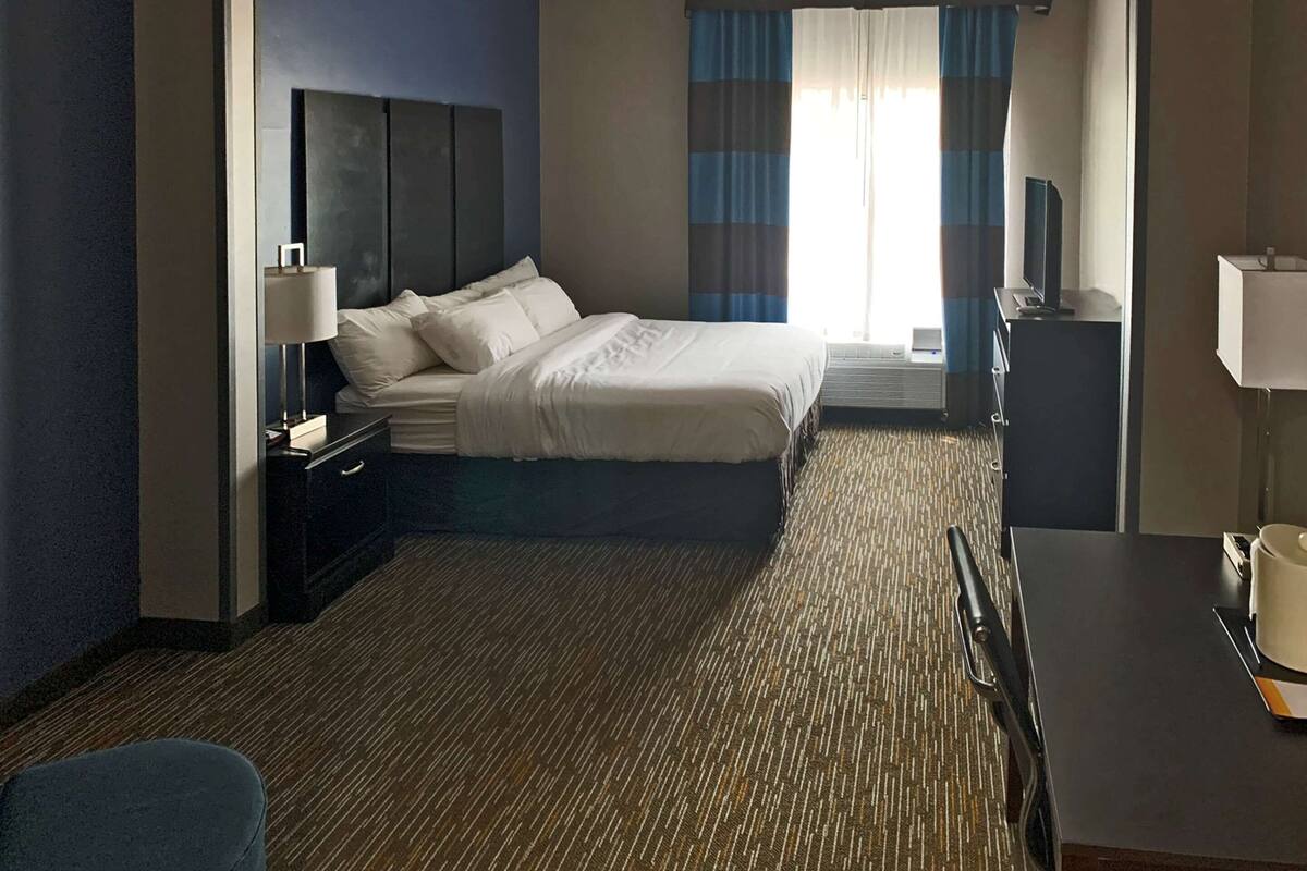 A hotel room with a bed, a desk, a chair, a TV, and a window with curtains.