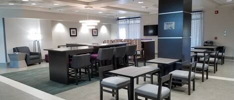 A modern hotel lobby with a reception desk, seating area, and a bar.