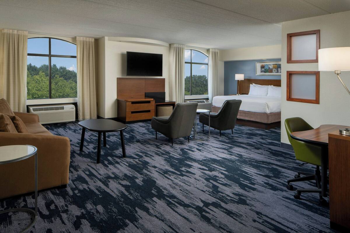 A hotel room with a bed, a TV, a desk, a chair, a sofa, and a view of the outdoors.